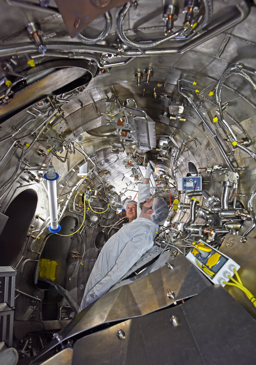 Arbeiten im Plasmagef&auml;&szlig;: Die bisherige Verkleidung mit Kohlenstoff-Kacheln
    ist entfernt; das Gef&auml;&szlig; ist bereit f&uuml;r den Einbau des neuen wassergek&uuml;hlten
    Wandschutzes.